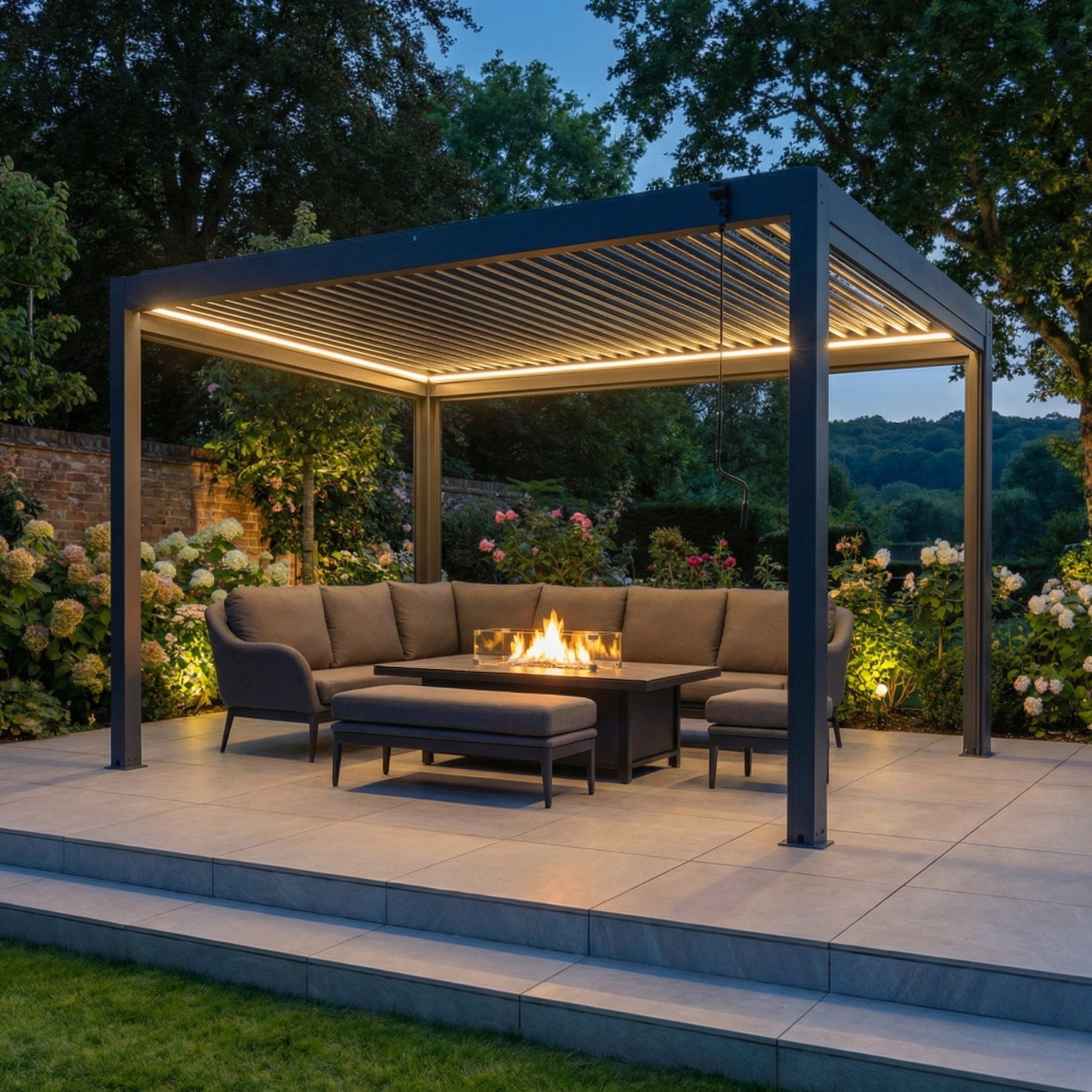 PergoSTET Plus 3m x 4m rectangular pergola with LED lighting in grey, paired with a gray outdoor sofa and fire pit table, creates a modern garden retreat at dusk.
