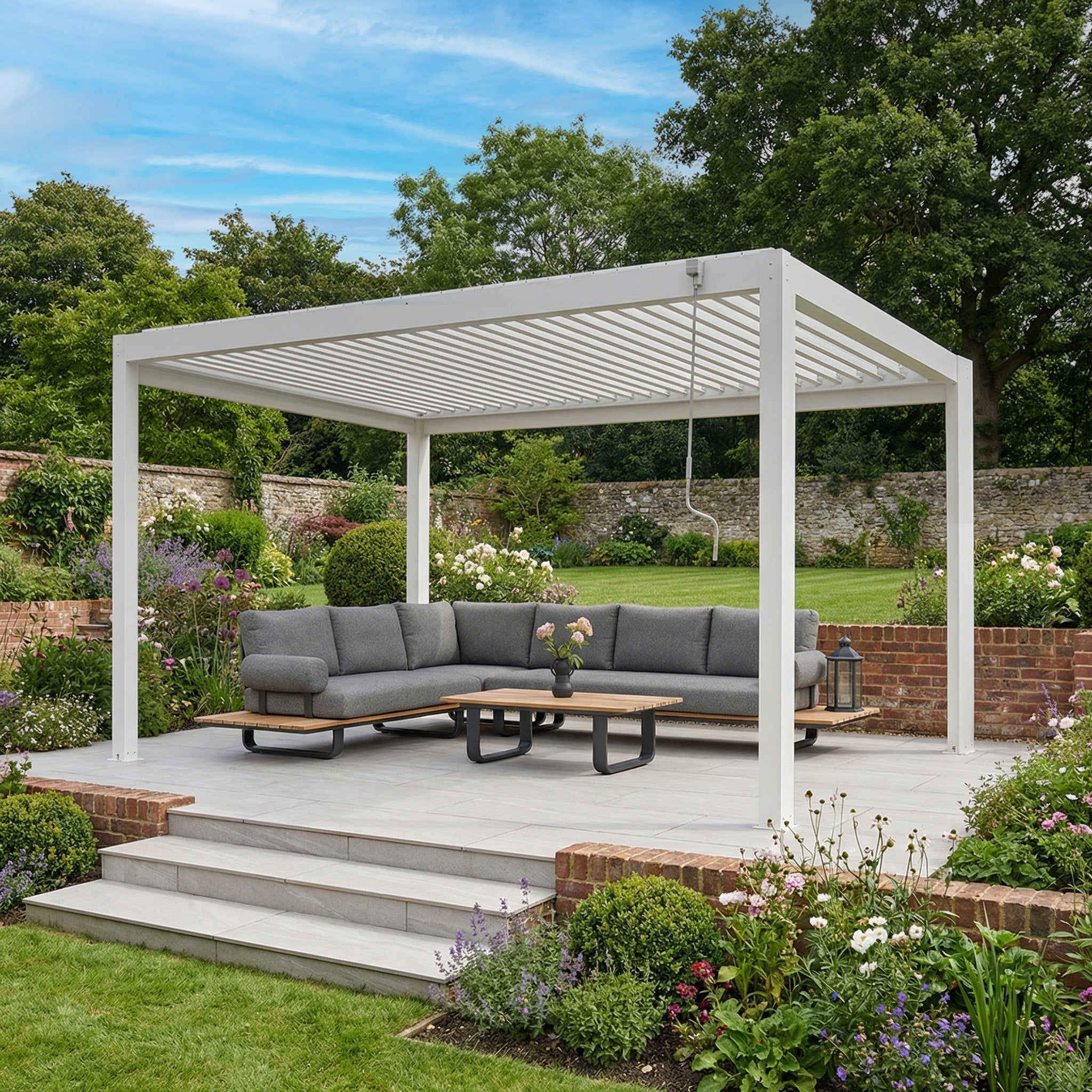 The PergoSTET Plus Frame Only 3m x 4m Rectangular Pergola with LED Lighting in White is shown on a patio with gray outdoor sofas and tables, surrounded by a lush garden.